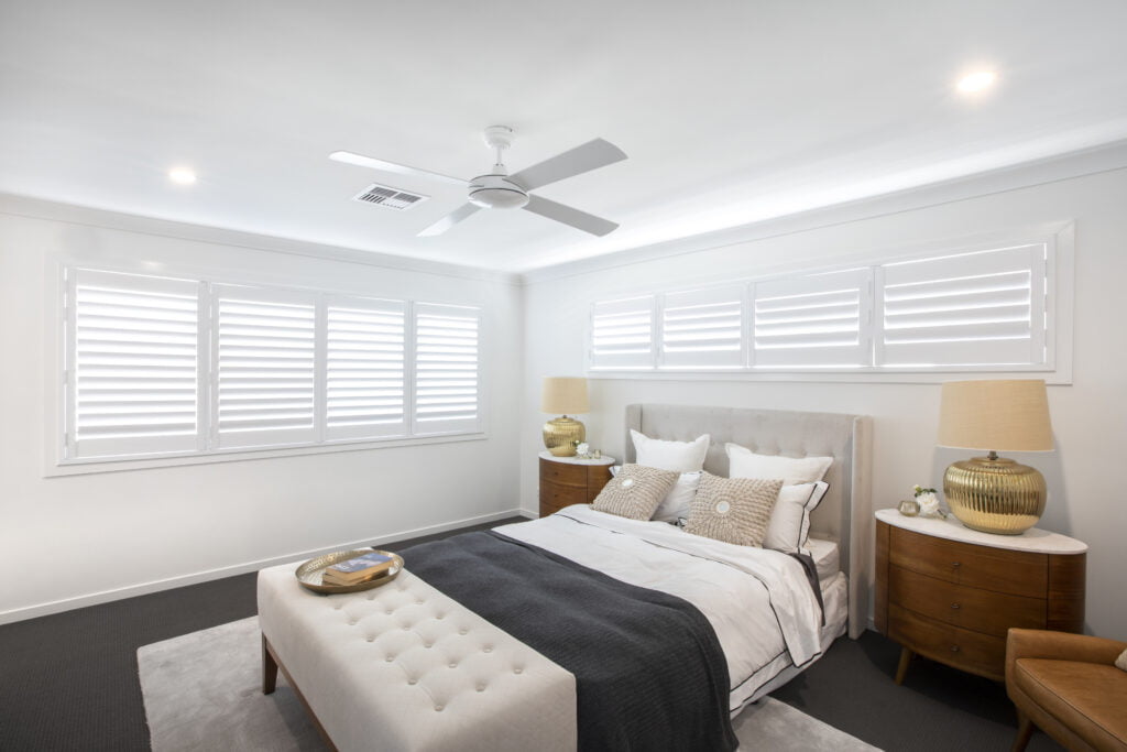White plantation shutters along the windows of a bedroom