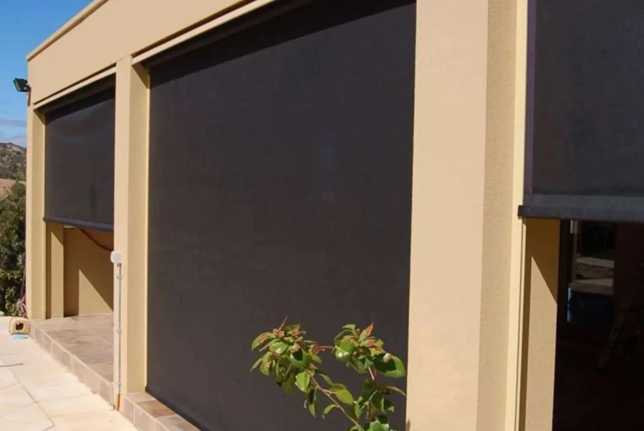 Dark Ziptrak blinds lowered between the rendered piers of an alfresco, each roller covered