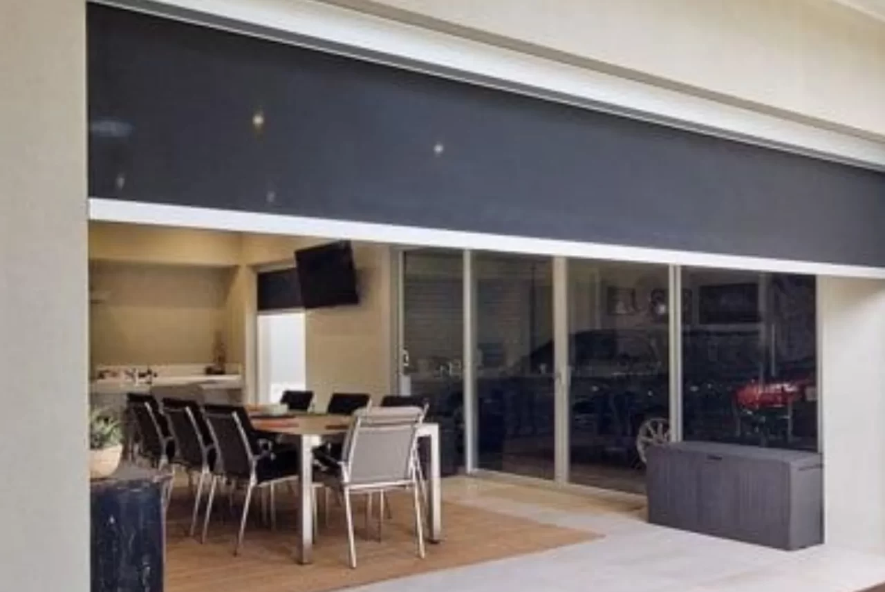 A wide Zipscreen blind raised above the opening between a dining room and a patio