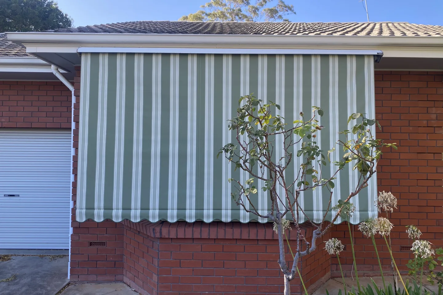 Green and white striped auto guide awning lowered over a bay window on a brick home