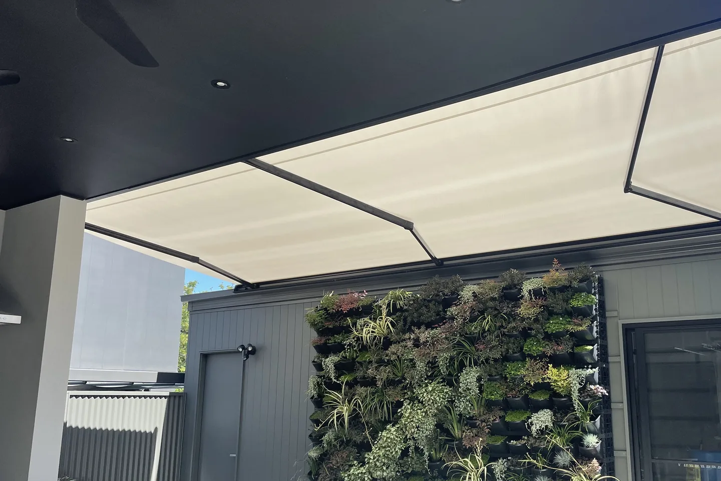 Cream folding arm awning extended over a courtyard beside a green plant wall