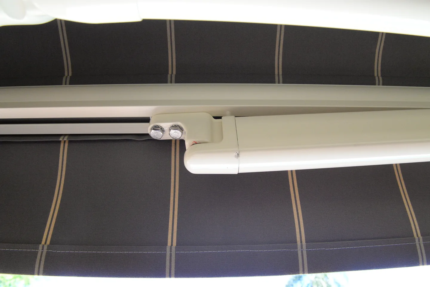 Close view of a folding arm elbow joint under a striped awning canopy