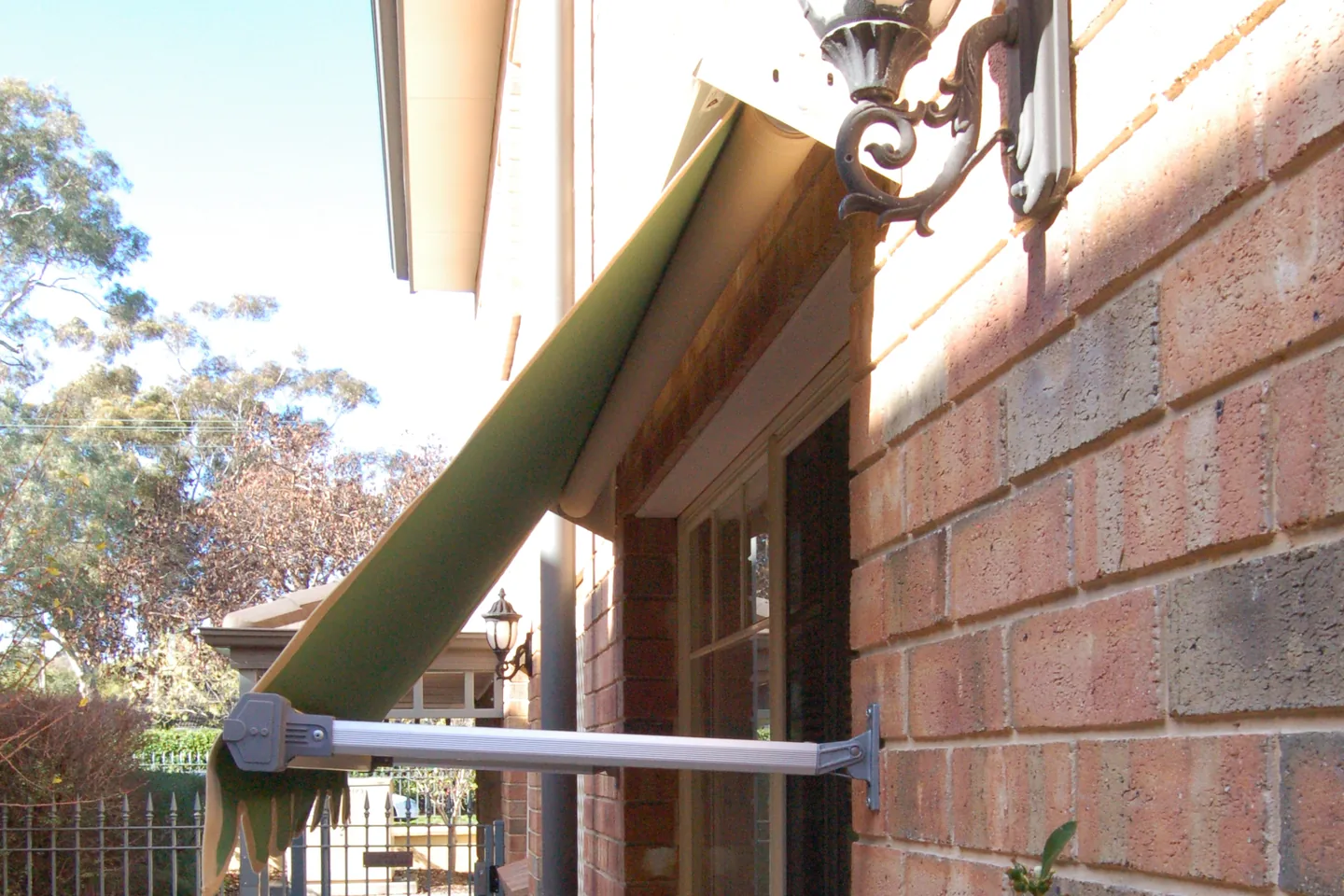 Pivot arm awning projecting from a brick wall with its arm and pivot bracket in view