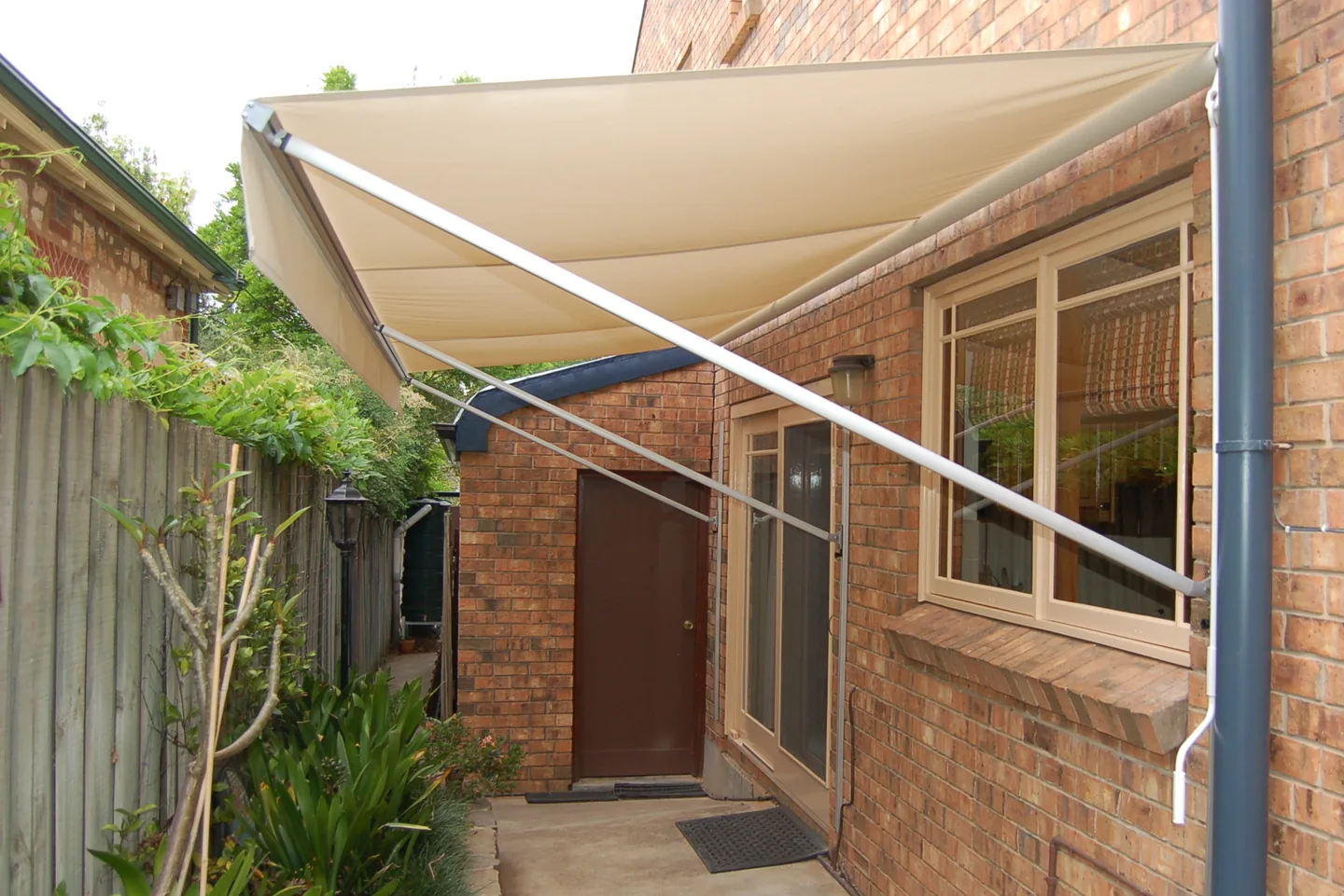 Long cream pivot arm awning projecting over a doorway along a brick side path