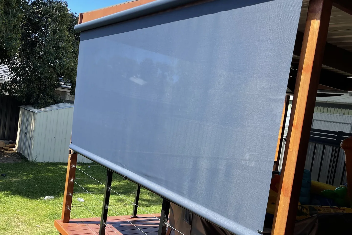 Charcoal straight drop awning lowered on the open side of a timber deck