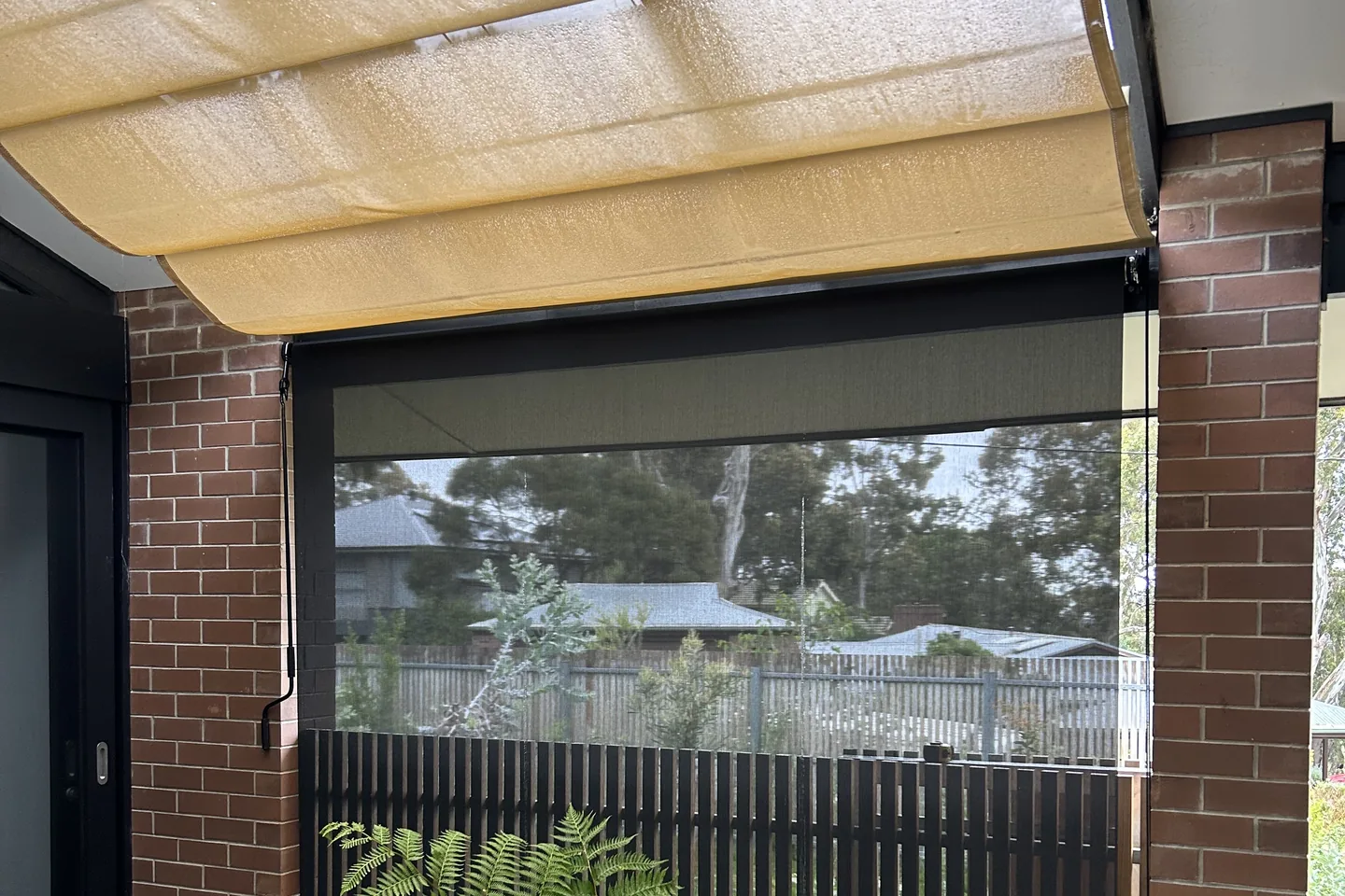 Straight drop awning lowered between brick piers under a pergola beside tree ferns
