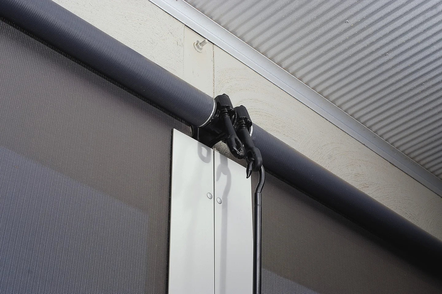 Close view of the roller and top bracket of a straight drop awning under a patio roof