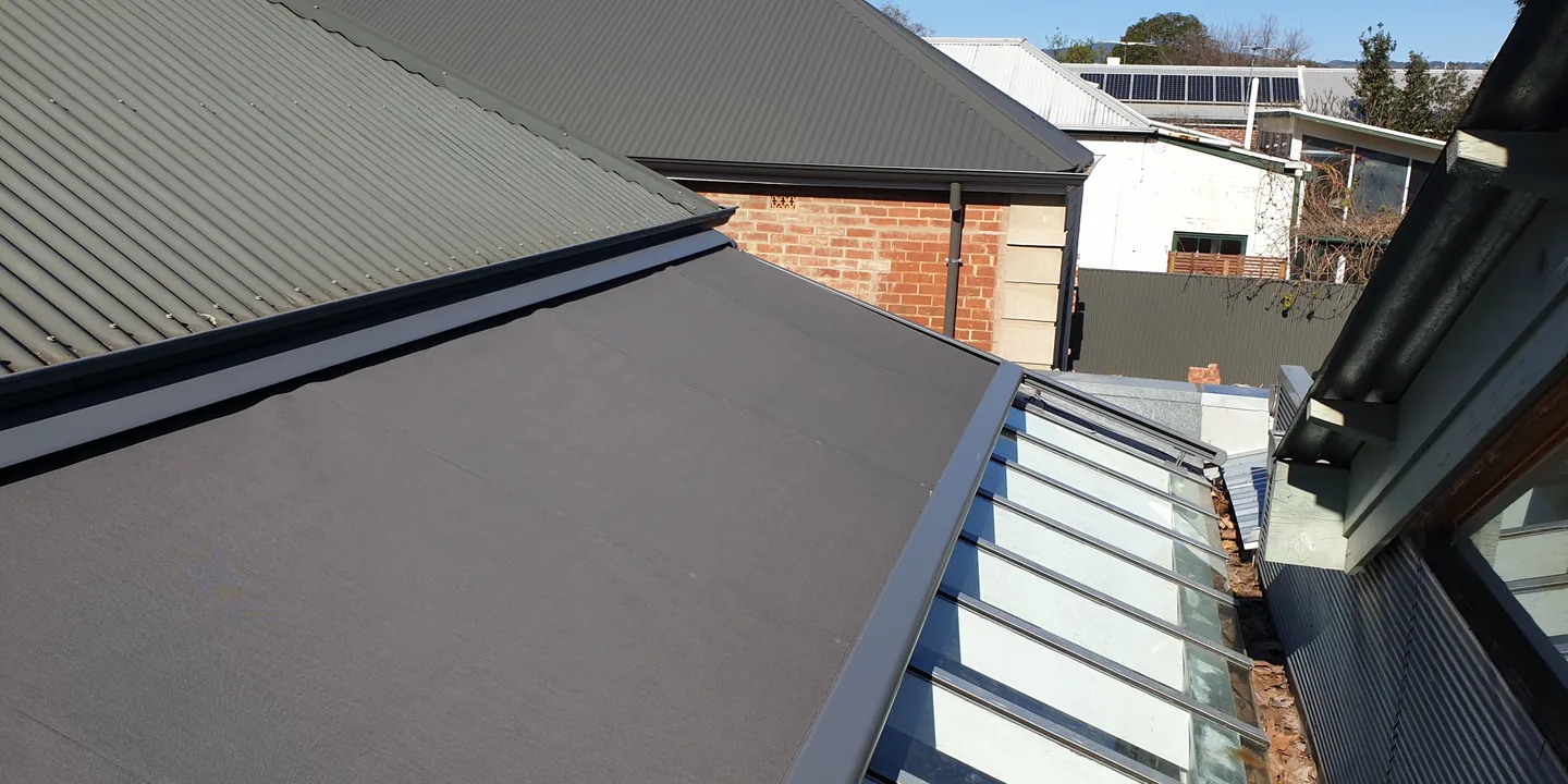 Charcoal Sundream roof awning extended across a glass-roofed extension between tin roofs