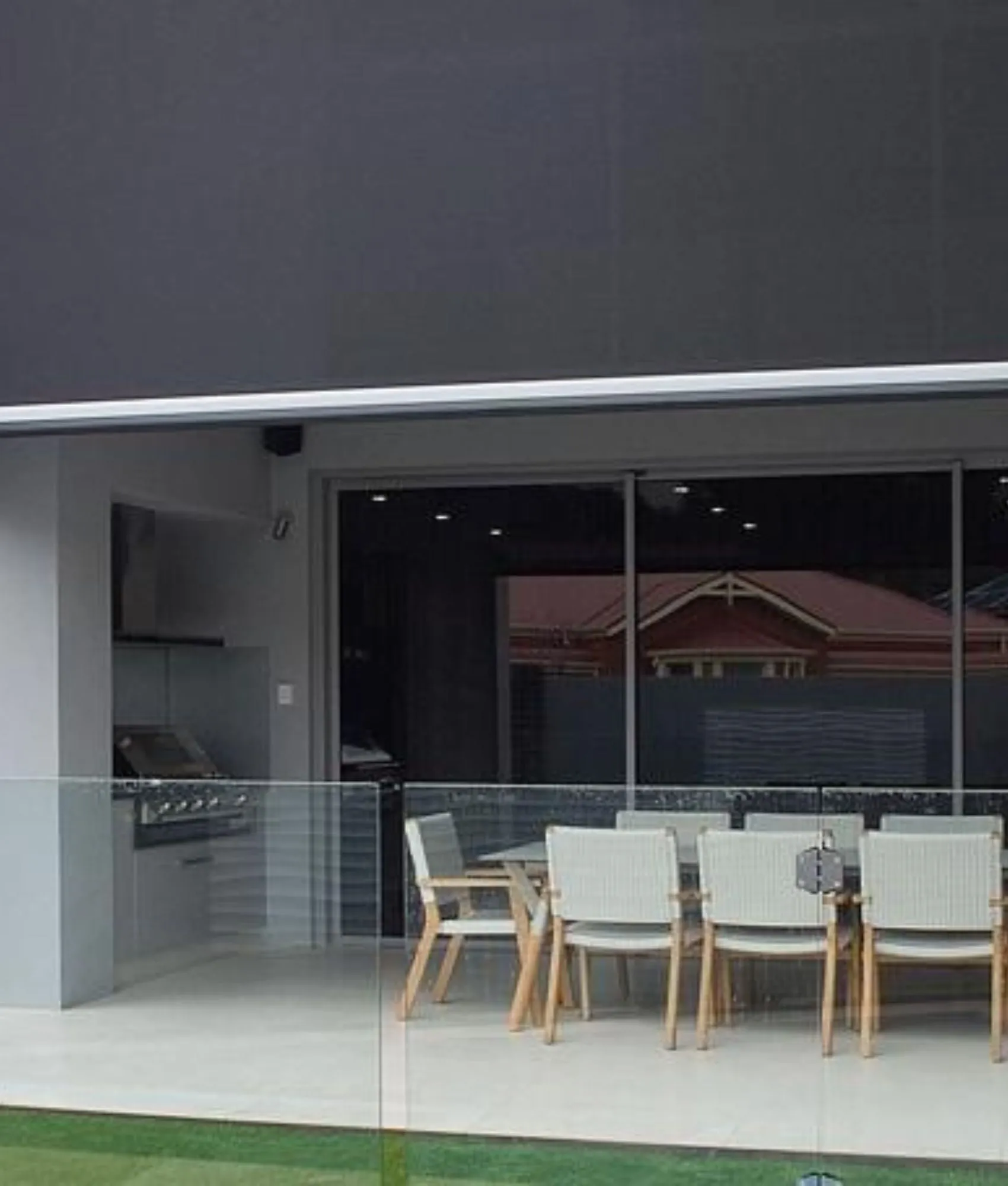 A charcoal Ziptrak blind raised part-way above an alfresco dining table and outdoor kitchen