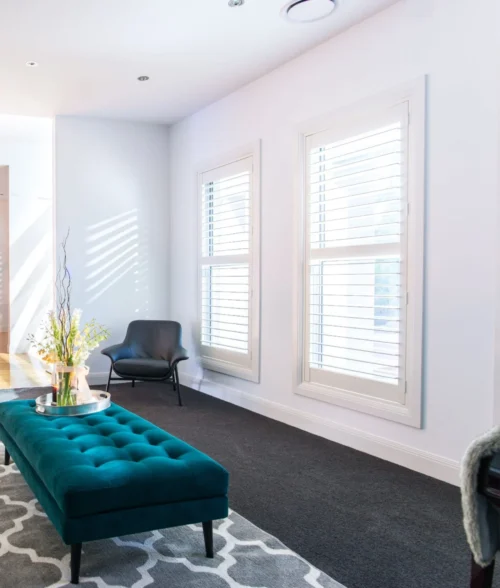 White plantation shutters in a living room with a teal ottoman