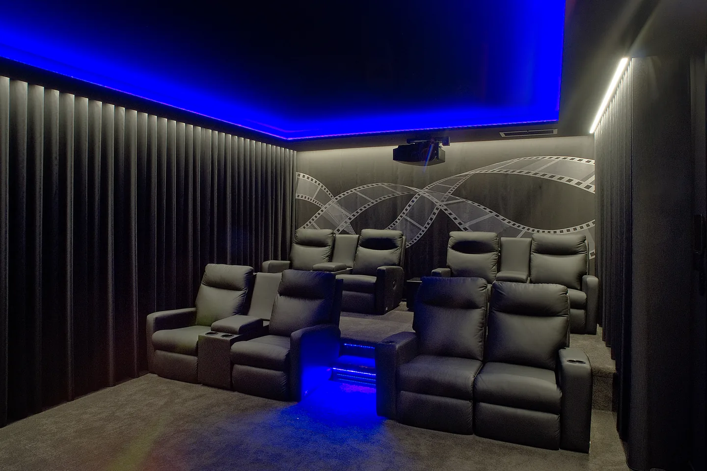 Home theatre lined with dark S-fold curtains under blue ceiling lighting