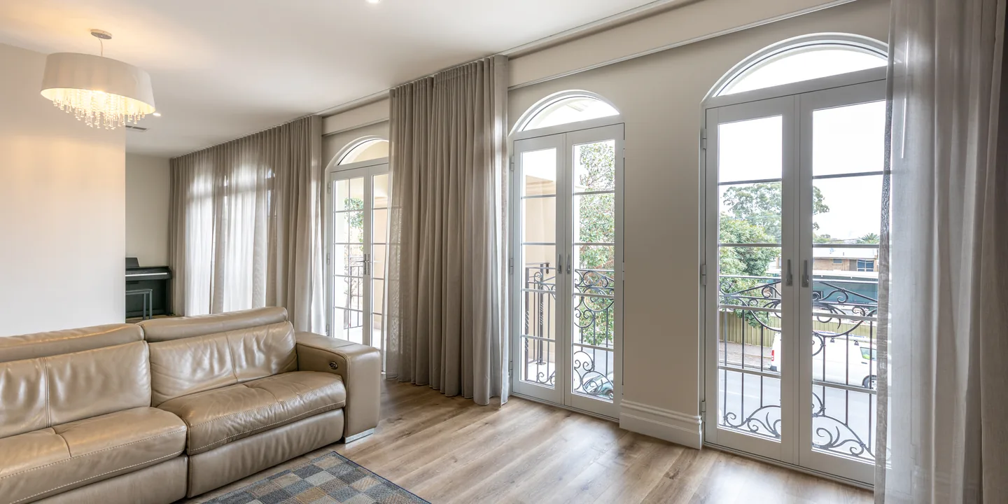 Floor-to-ceiling S-fold curtains and sheers either side of arched French doors in a living room