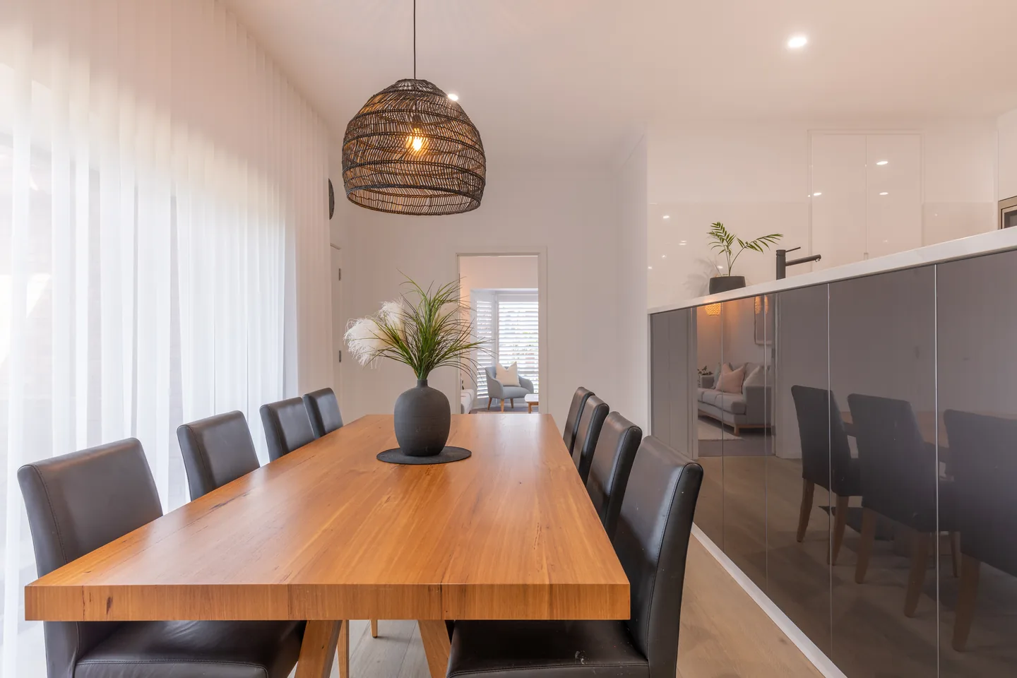 Dining area with white sheer curtains softening daylight along a wall of windows