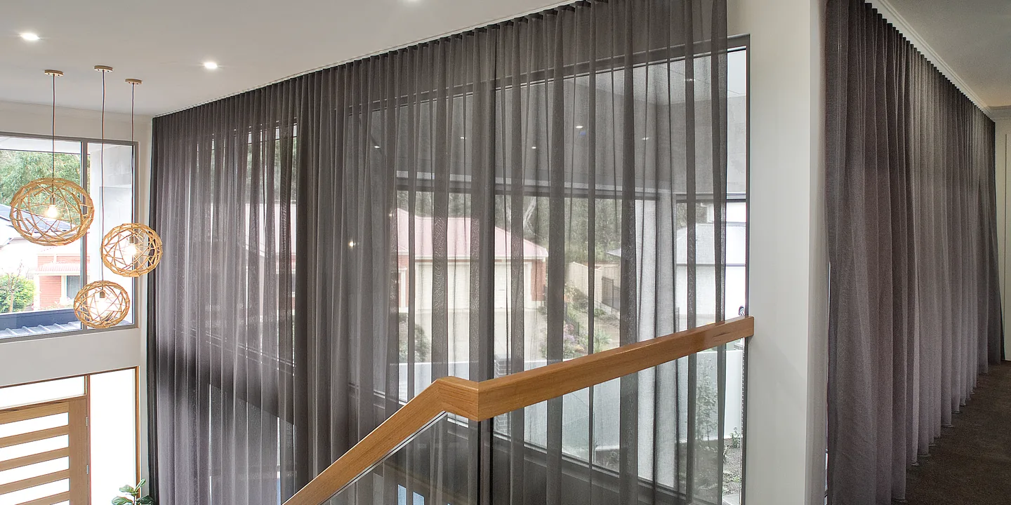 Full-height charcoal sheer curtains across a double-height stairwell window