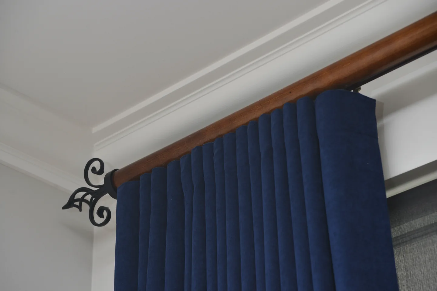 Navy pleated curtain hanging from a timber rod with a black iron finial