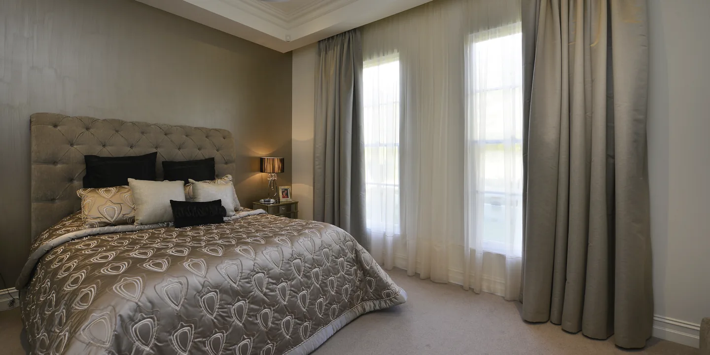 Bedroom with full-length pleated drapes and sheers across tall windows
