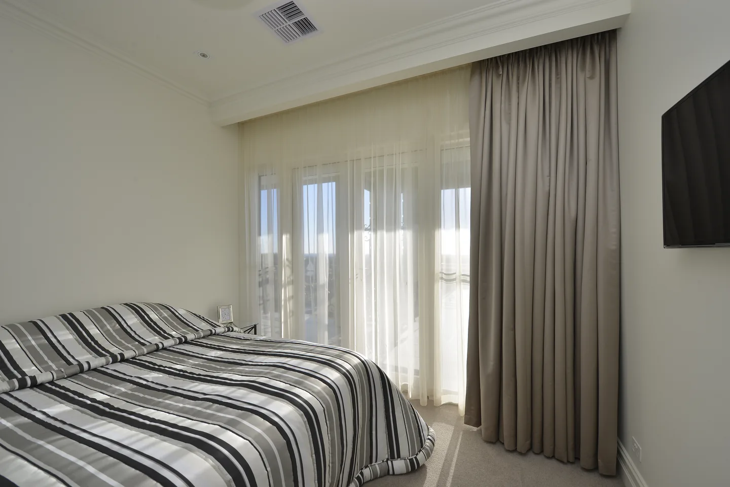 The same bedroom with the drapes stacked to one side and sheers across the doors