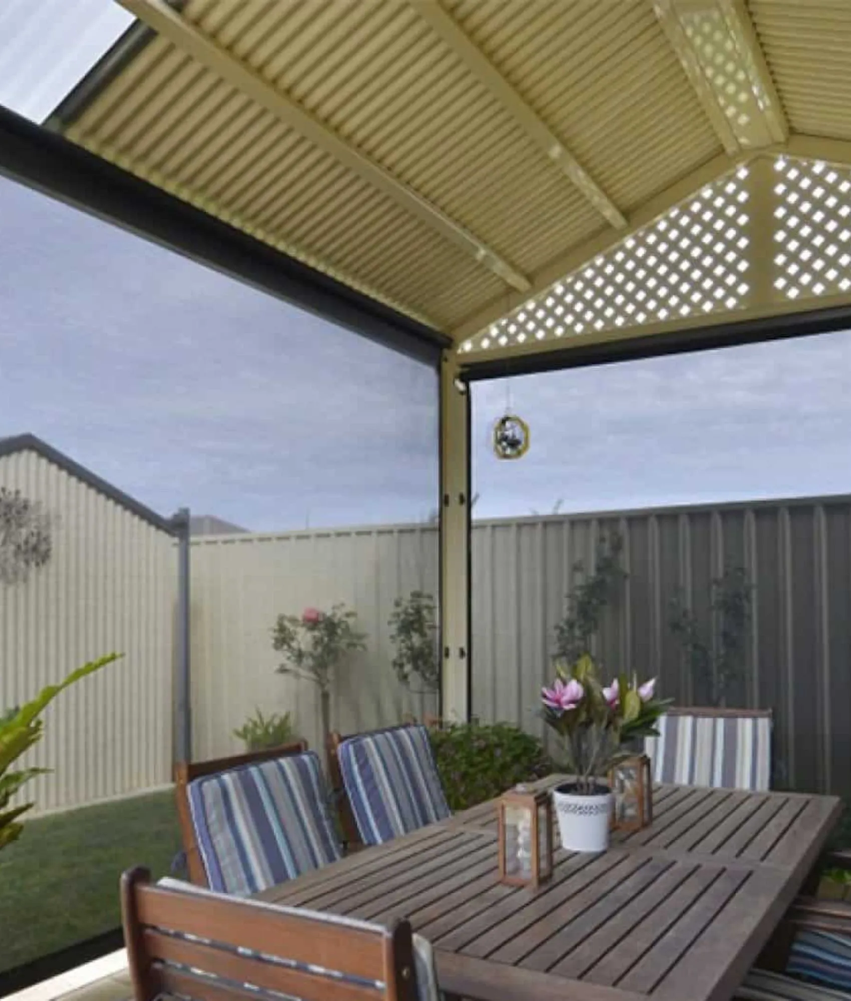 Mesh Ziptrak blinds lowered along two sides of a gable-roofed patio with a timber dining setting