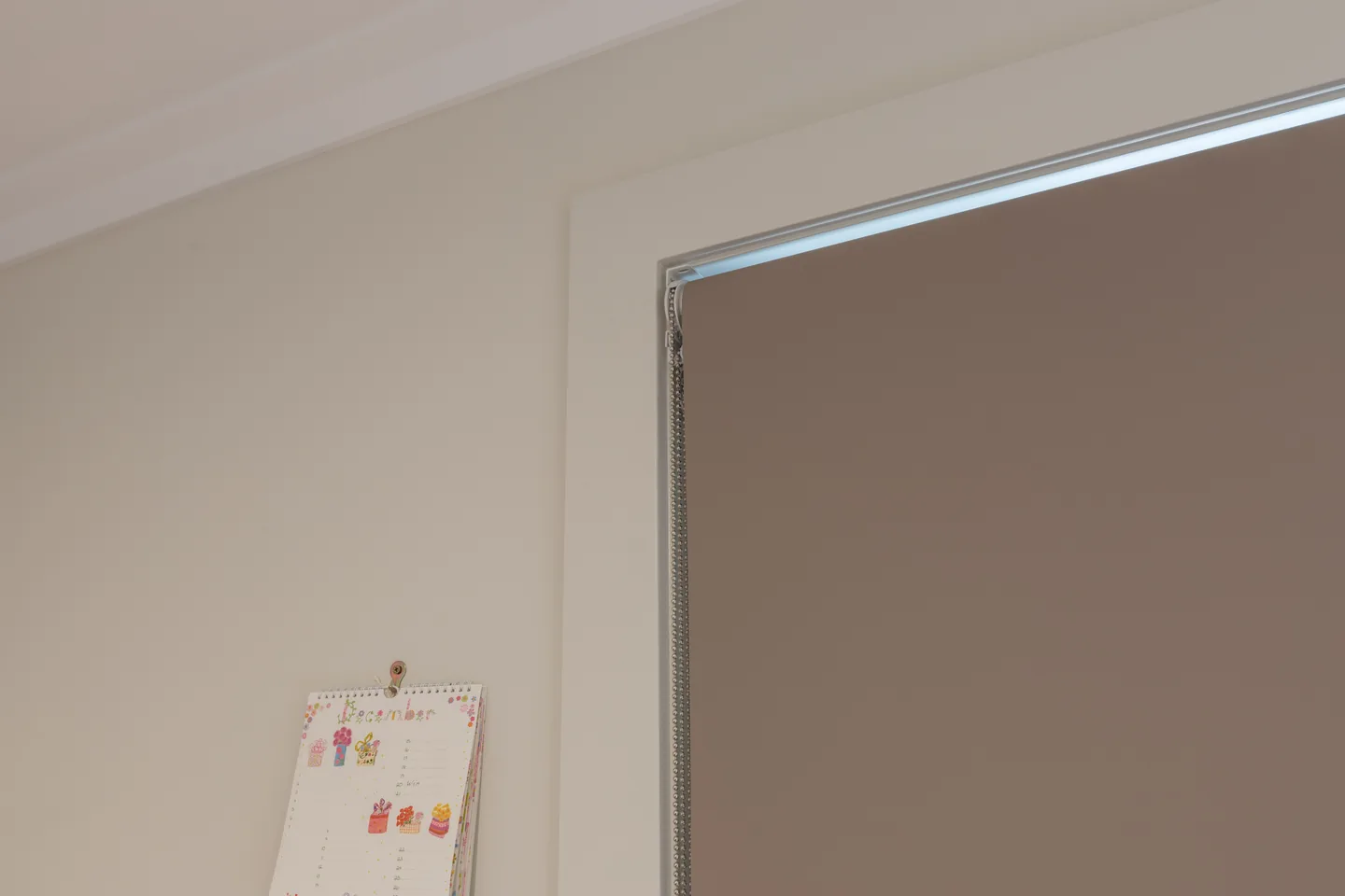 Dark blockout roller blind lowered close to the wall, with its side edge and chain in view