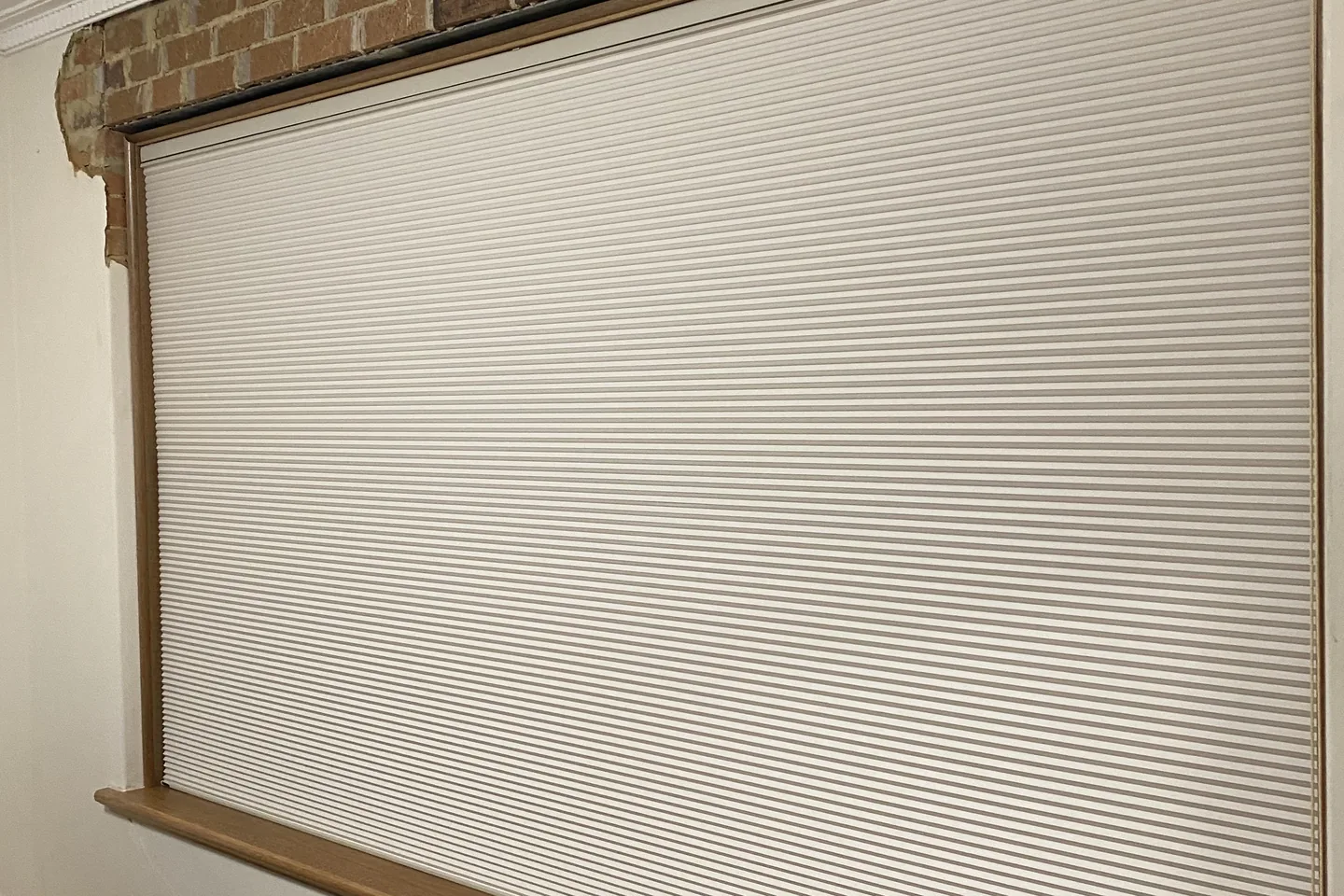 Wide window under a brick lintel with a white honeycomb blind fully lowered