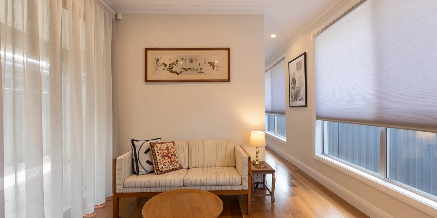 Sitting room with a white honeycomb blind lowered over a long window beside sheer curtains