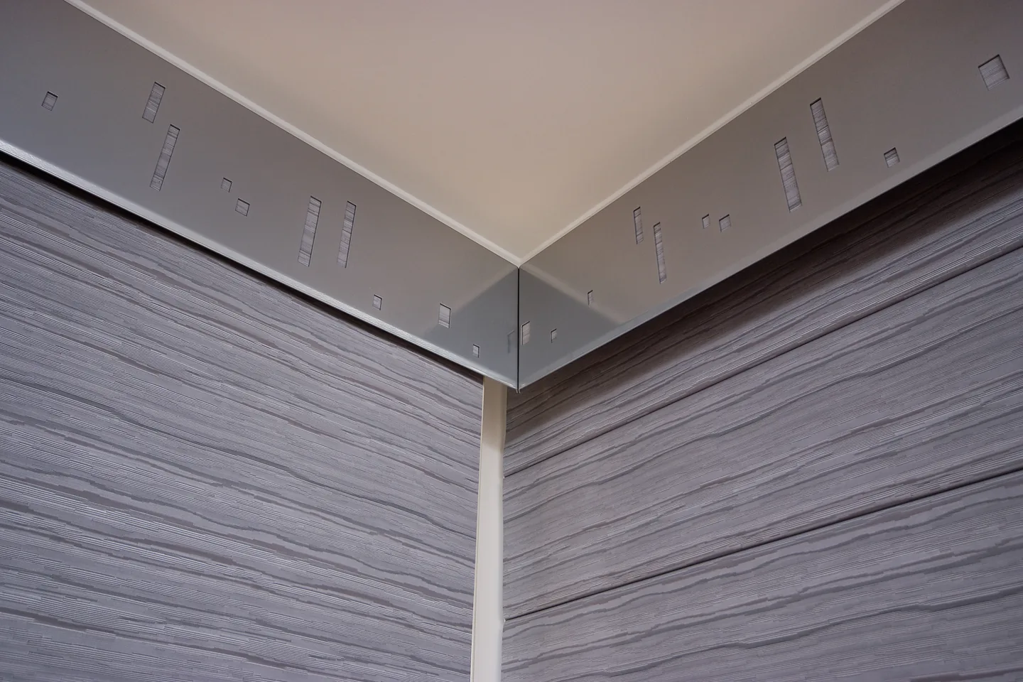 Two runs of textured fabric panels meeting at a room corner beneath a metal pelmet