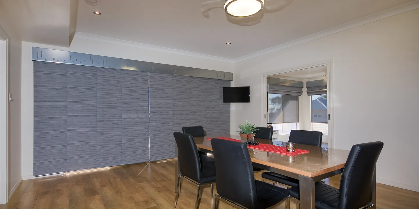 Grey textured panel glide blinds closed across a wall of sliding doors beside a dining table