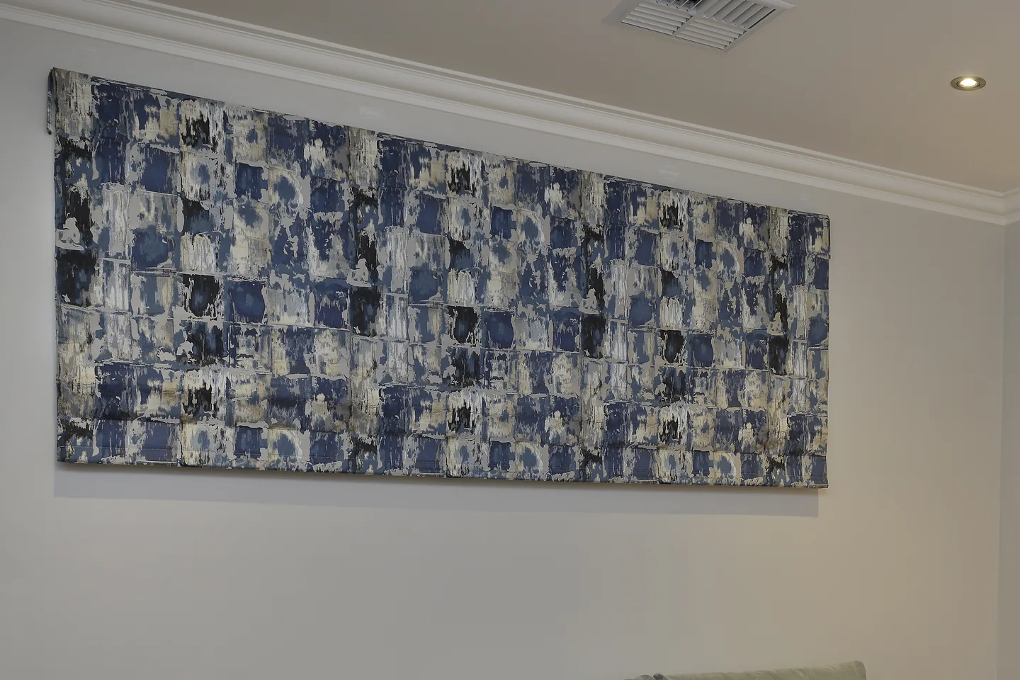 Blue and white patterned Roman blind raised over a wide bedroom window