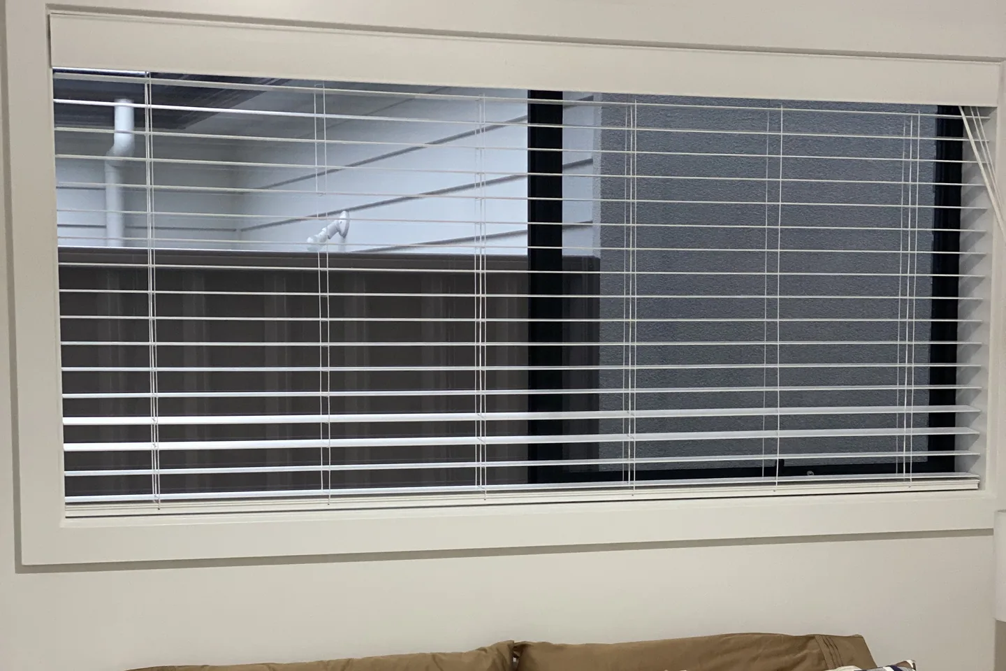 White aluminium Venetian blind installed in a wide bedroom window above the bed