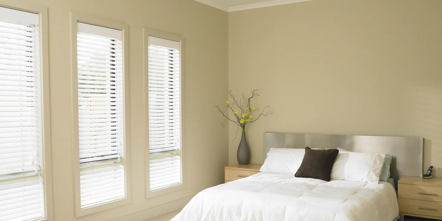 Bedroom with white timber Venetian blinds on three tall windows, slats tilted open