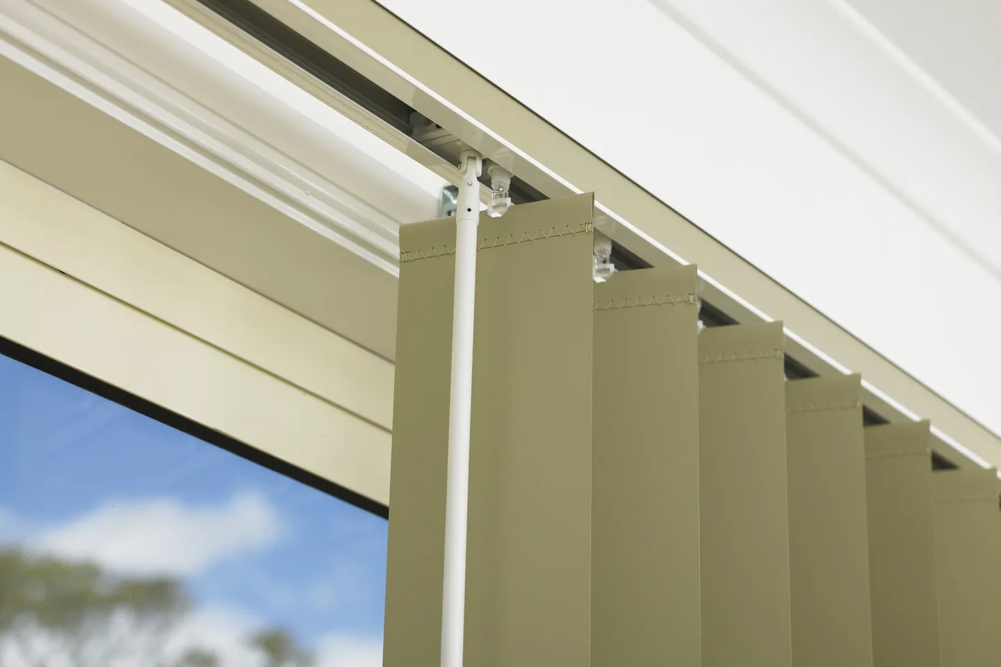 Close view of a vertical blind headrail with vane carriers and the wand control