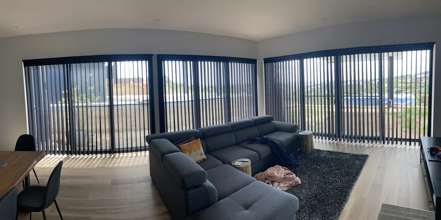 Open-plan living room with dark vertical blinds across a long corner run of windows, vanes open to the view