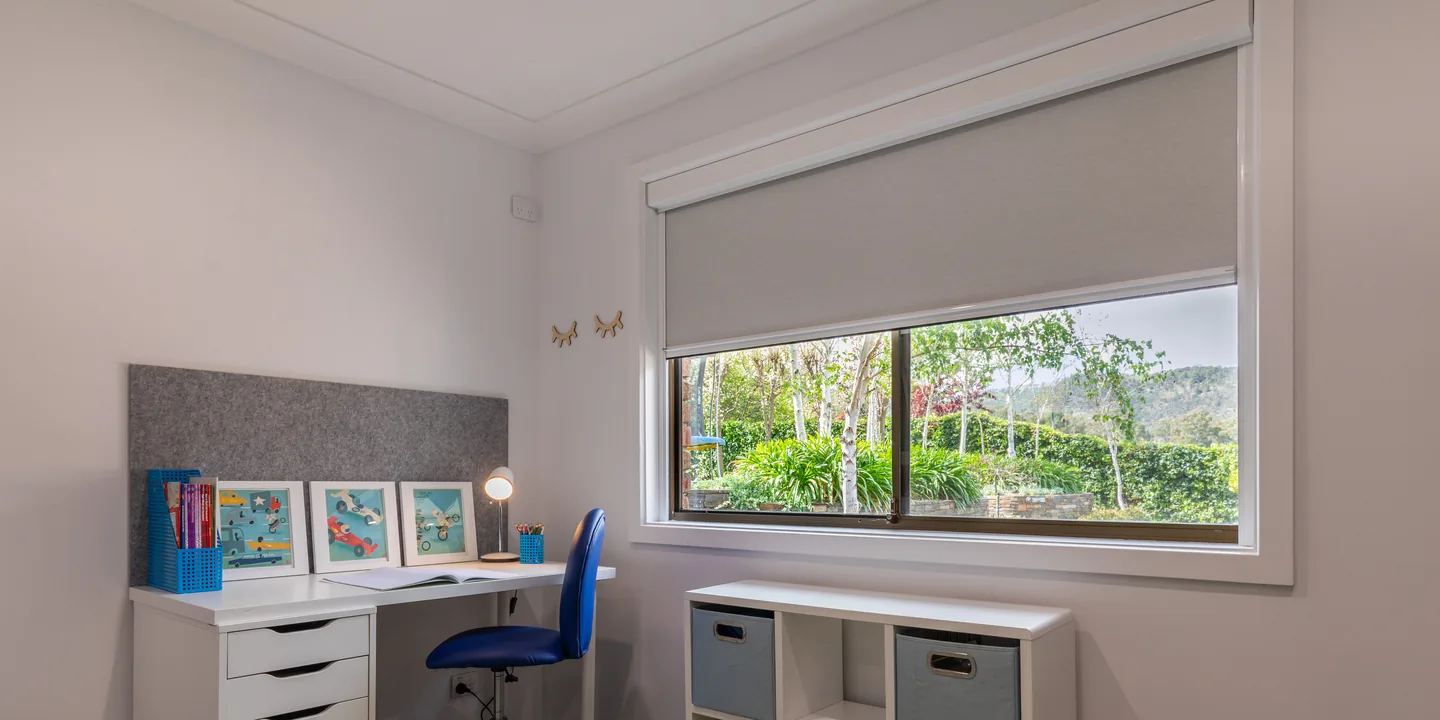 Study with a light grey Ziptrak Interior blind half lowered in its side tracks over a garden window