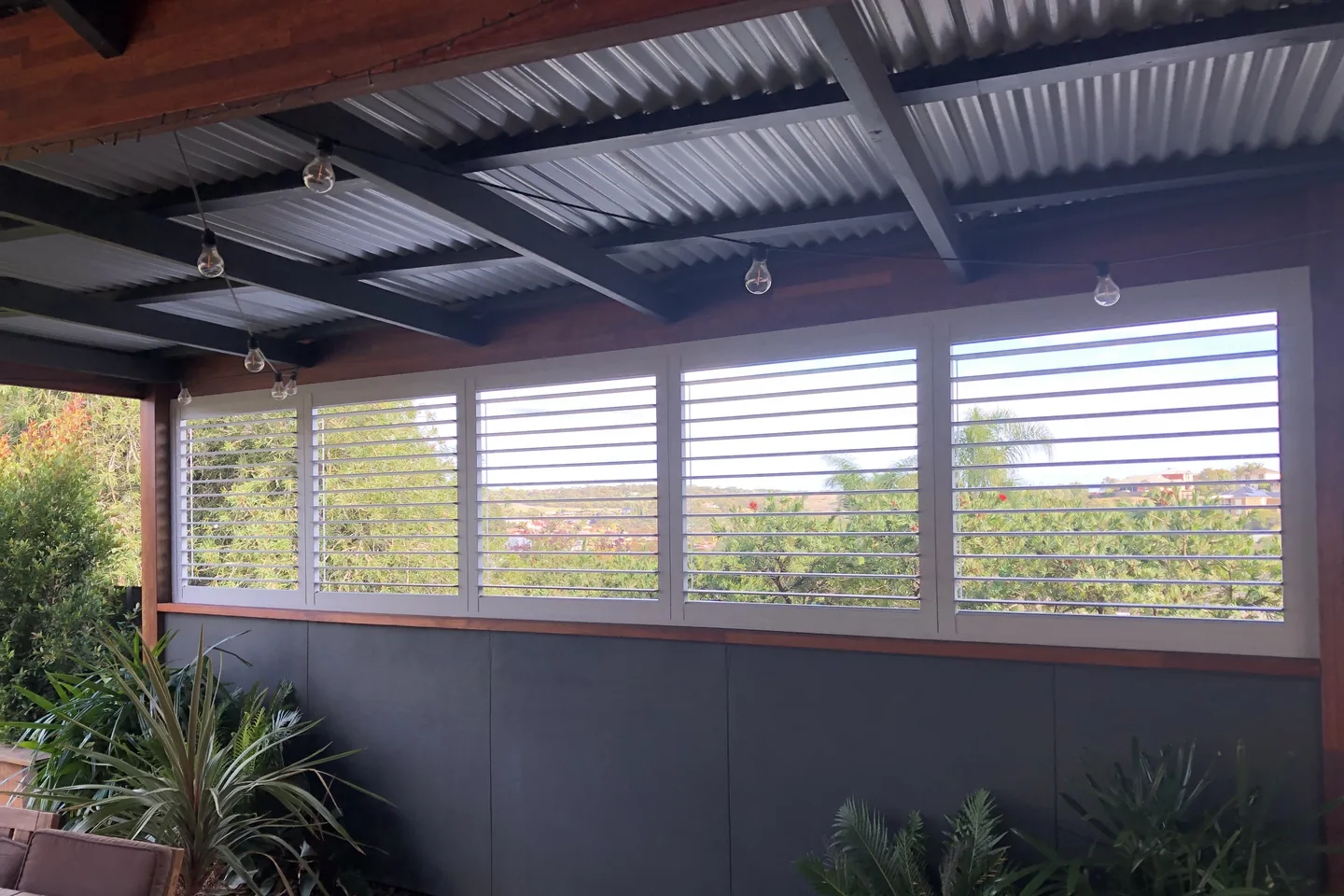 Outdoor plantation shutters enclosing the upper half of a verandah, with louvres open to the garden view
