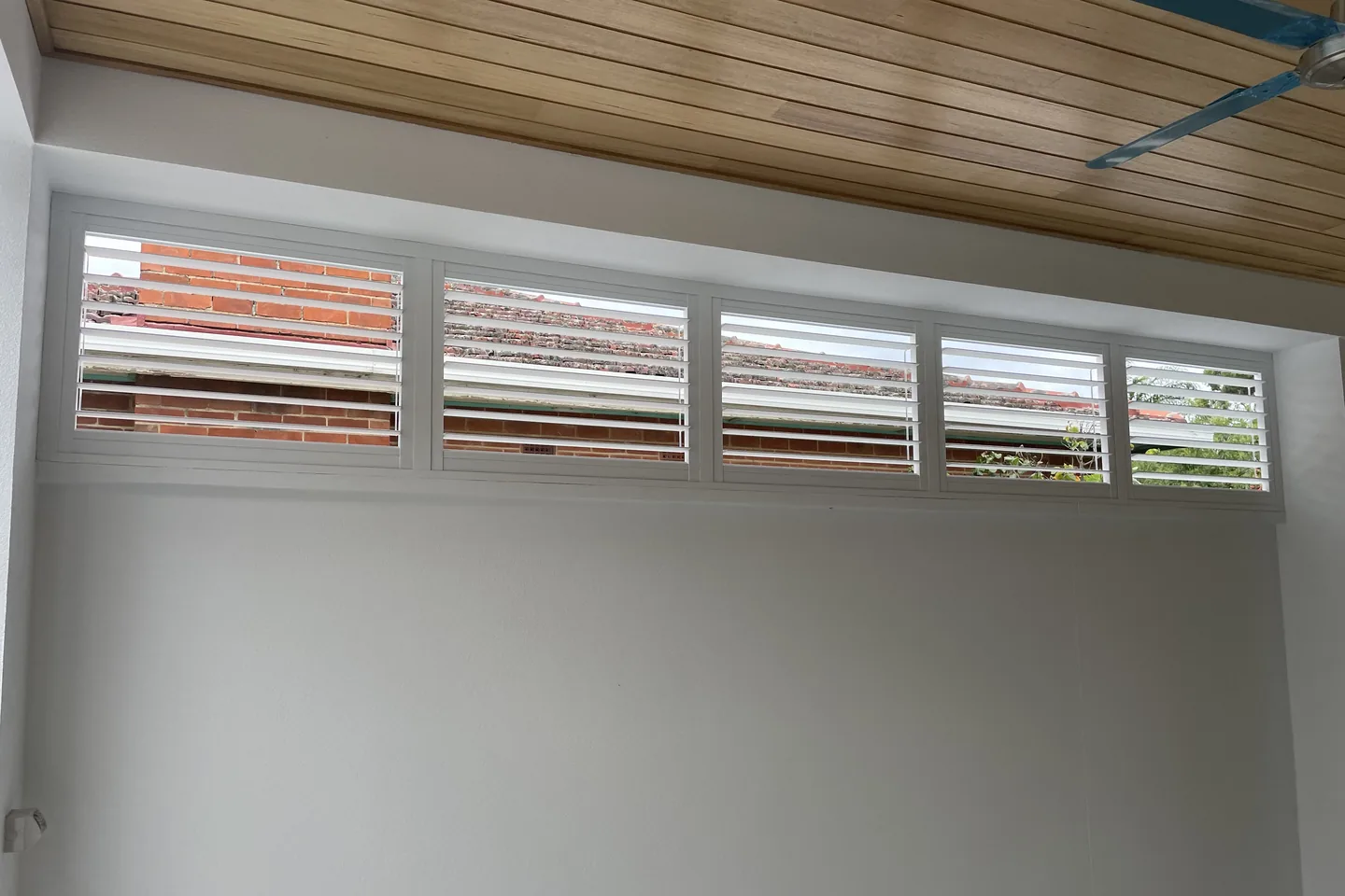 Row of shutters fitted to high openings in an alfresco under a timber-lined ceiling