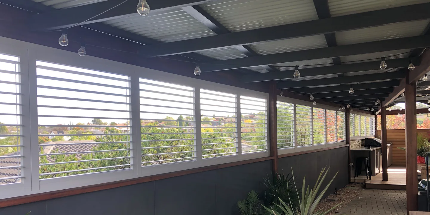 White plantation shutters running the length of a covered verandah above a dark half wall