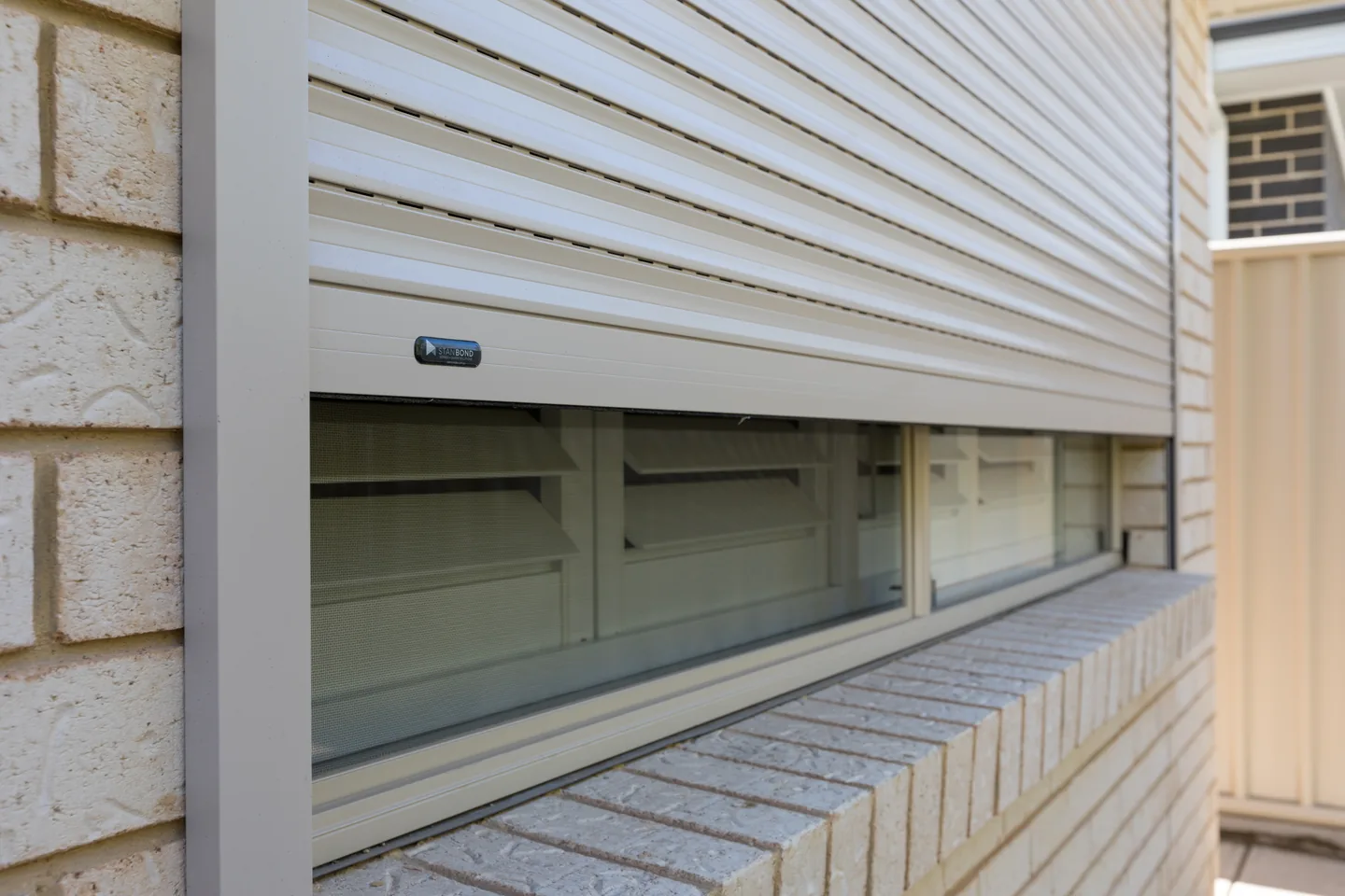 Roller shutter partly raised, showing the bottom rail above a window sill