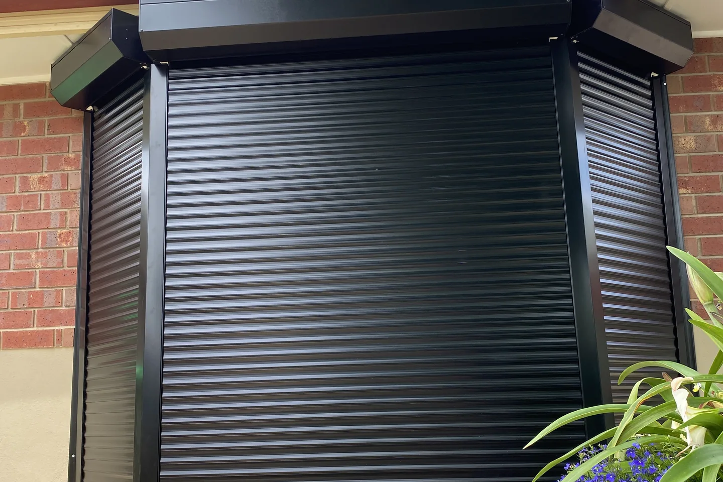 Black roller shutters lowered around a brick bay window with angled side sections