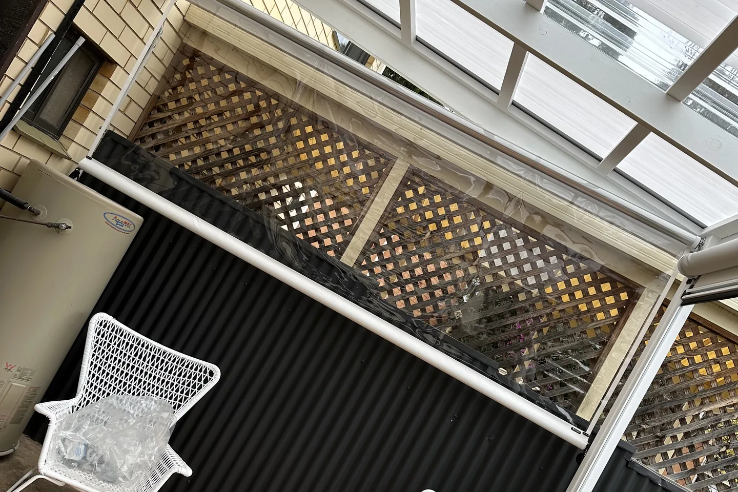 Clear outdoor blind and its white bottom rail above a dark balustrade, seen from the corner of the same deck