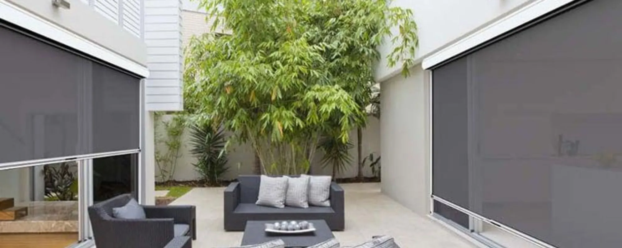 Charcoal Ziptrak outdoor blinds on both sides of a paved courtyard with an outdoor lounge