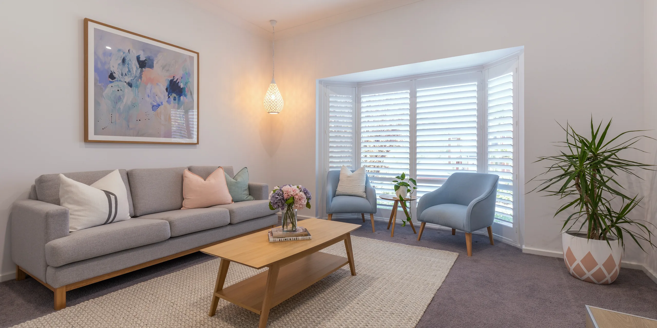 Living room with white plantation shutters across a bay window, louvres tilted open