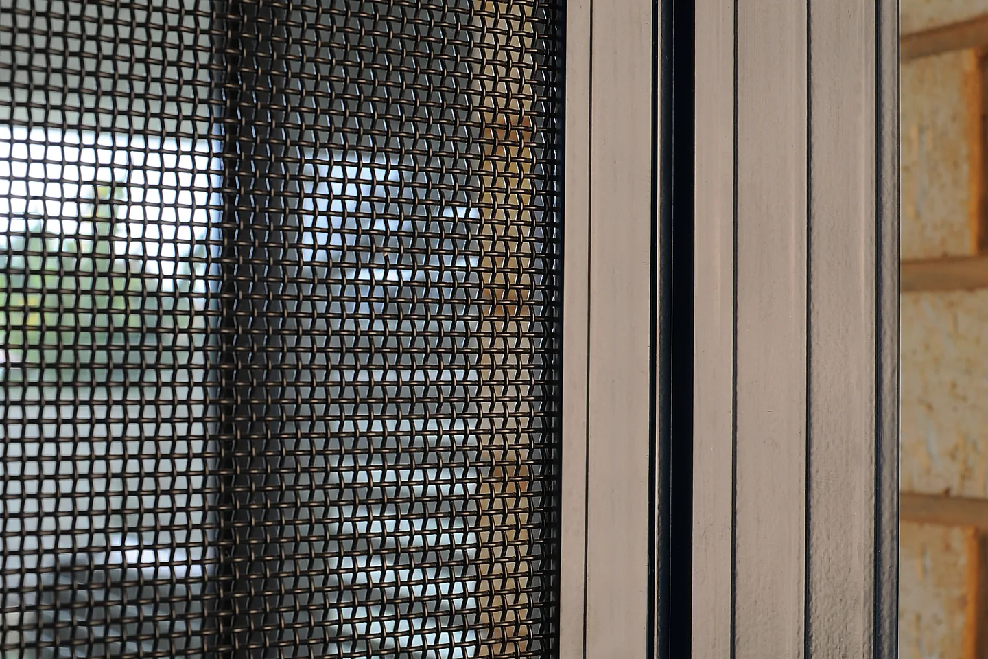 Close view of black stainless steel mesh held in a black door frame with screws along the edge