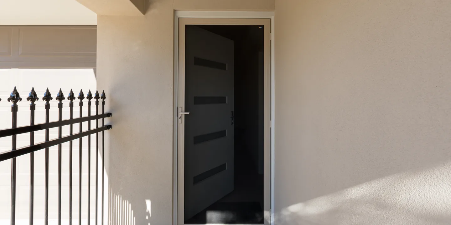 Crimsafe stainless steel mesh security door in a cream frame across a rendered front entry, beside a black spear-top fence