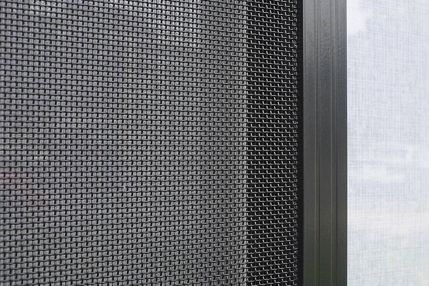 Close view of woven stainless steel security mesh beside a black aluminium frame
