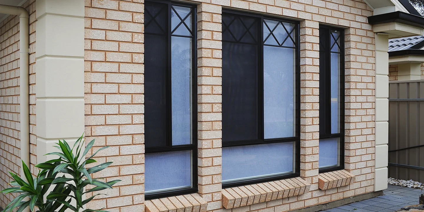 Three windows on a cream brick home fitted with dark stainless steel mesh security screens