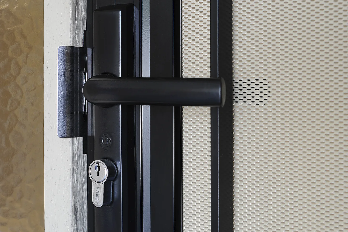 Lever handle and keyed lock on a black security door with a perforated aluminium screen