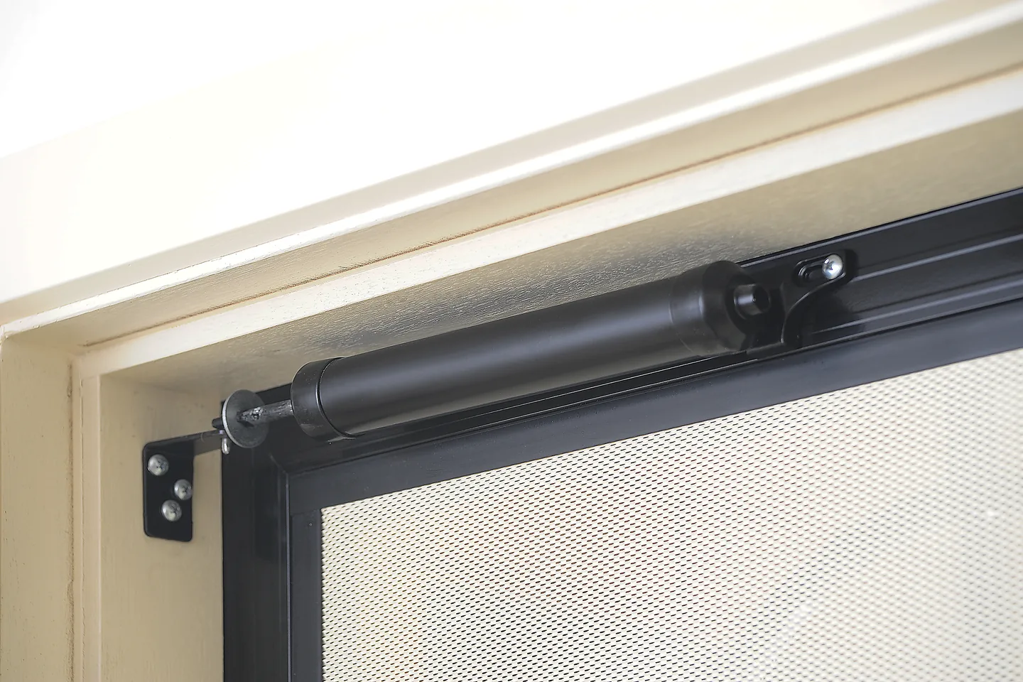 Door closer mounted on the top rail of a black security door with a perforated screen