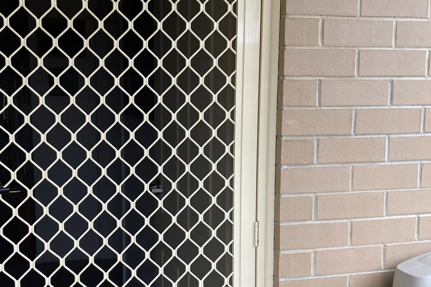 Cream diamond grille security door at a brick front entry