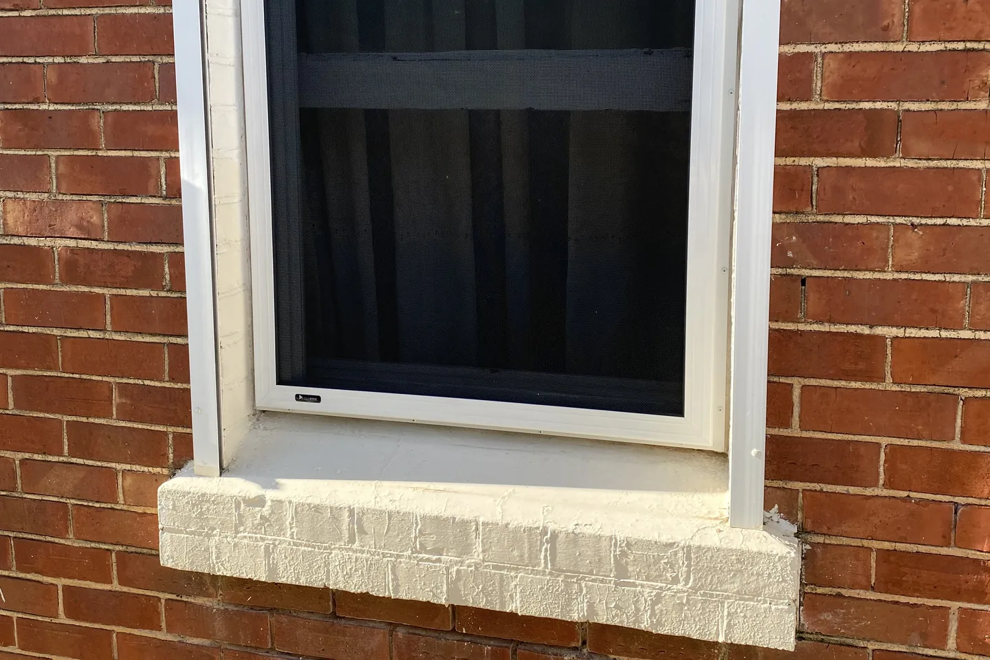 Mesh security screen fitted over a double-hung window in a red brick wall