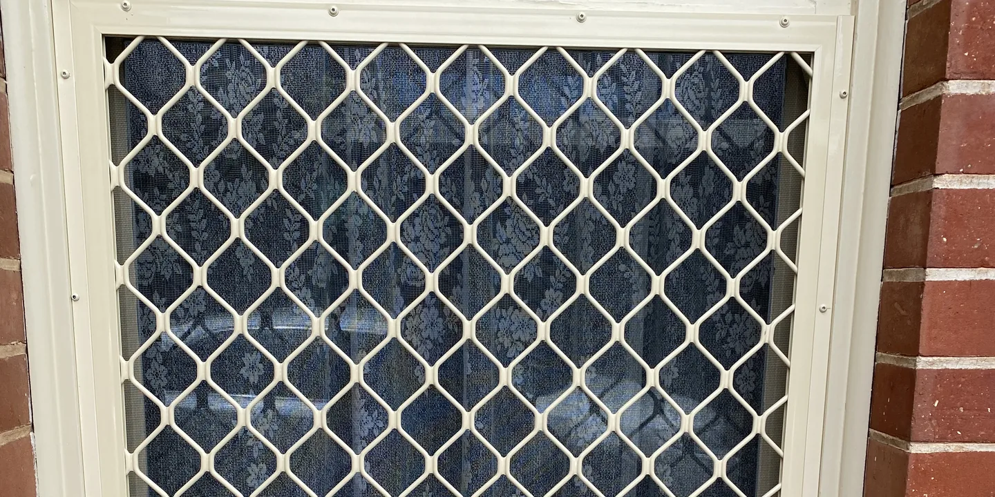Cream diamond grille security screen fitted over a window in a red brick wall